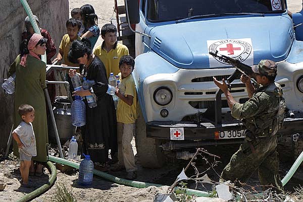 Ethnic Uzbek refugees collect water as a Kyrgyz soldier on patrol gives them the OK in the village of Suratash, Kyrgyzstan, on Sunday.