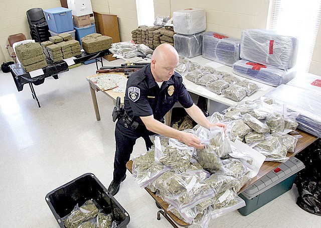 North Little Police Department property officer Brian Mitchell packs away bags of marijuana Monday afternoon after a news conference to show off the drugs, weapons and cash seized in an interagency drug bust Sunday.