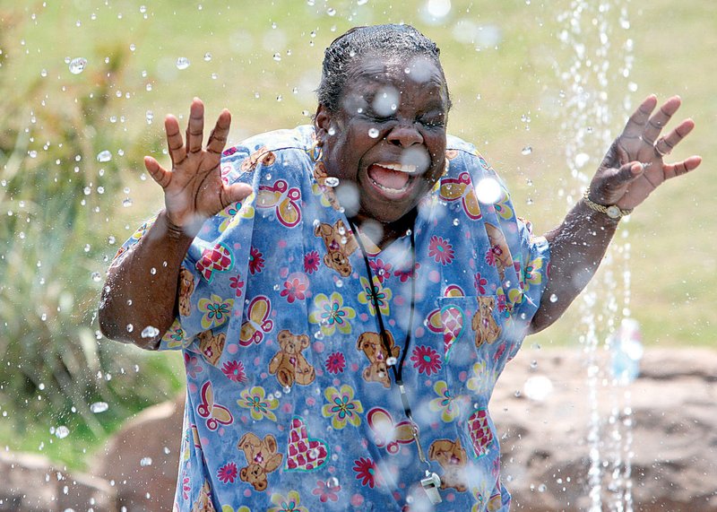 Thelma Triplett, an assistant teacher at Bright Ideas Enrichment Center, shrieks Tuesday morning as she passes through the fountain at Little Rock’s Riverfront Park while playing with some of her students during a field trip to the park.