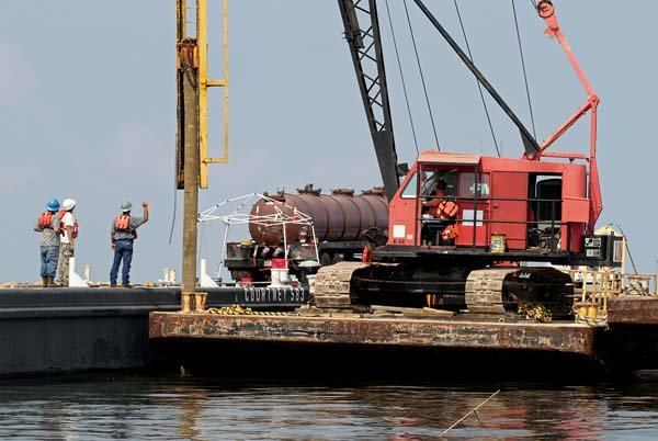 Workers drive a pole into place Monday in Pass Abel, near Grand Isle, La. The pole will keep several barges, which will be lined up end to end, in place to serve as a barrier against oil.