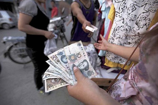 A Chinese woman who sells clothing on the roadside in Beijing carries a handful of yuan on Tuesday. 