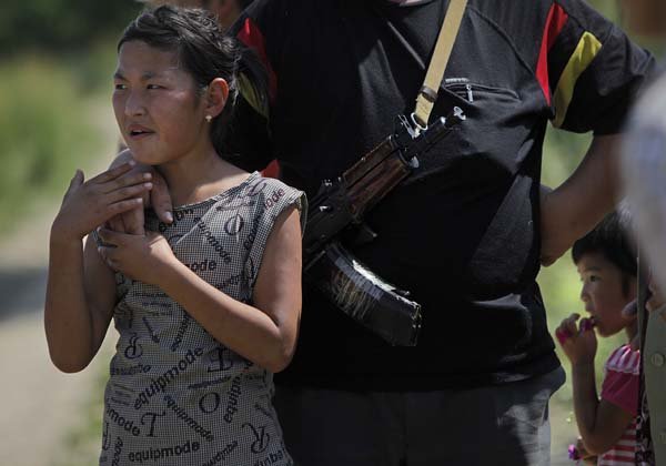 A girl is comforted Wednesday by an armed security guard as Kyrgyz unload Russian humanitarian aid from the Siberian city of Krasoyarsk at a camp housing Kyrgyz refugees outside the southern Kyrgyz city of Osh.