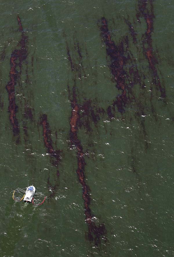 A boat pulls absorbent materials along the surface of the Gulf of Mexico among large streaks of oil Sunday near Venice, La.