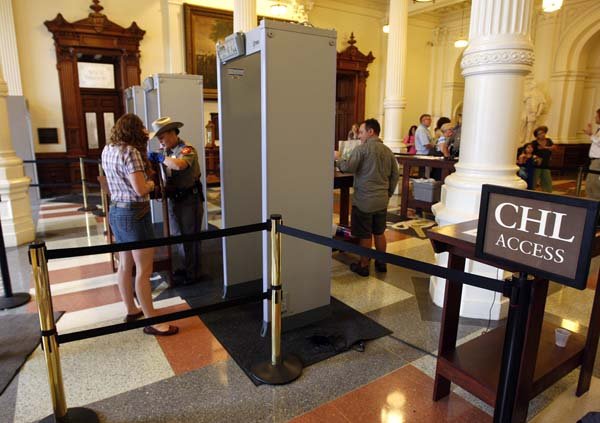 People pass through metal detectors in June at the Texas Capitol in Austin, near a sign marking where those with concealed handgun licenses can bypass the detectors.