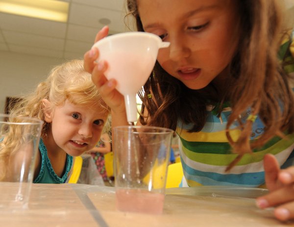 Abby Lawson, 6, winces as Savannah Pledger, 7, pours water through a filter while the two were taking part in the Invention Camp on Tuesday at Leverett Elementary School in Fayetteville. The exercise required campers to find ways to clean up water dirtied with household items using filters in order to learn about pollution.