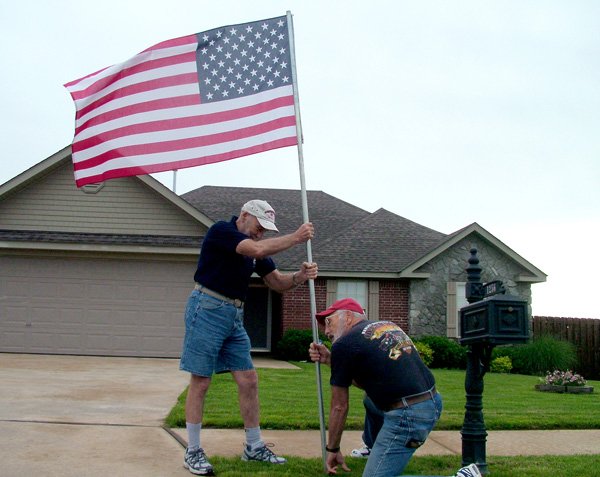 Flags flying in neighborhoods around town are erected by members of the Pea Ridge Optimist Club. Members Bill and Faye Ryan, brothers, placed this flag in Standing Oaks subdivision recently.