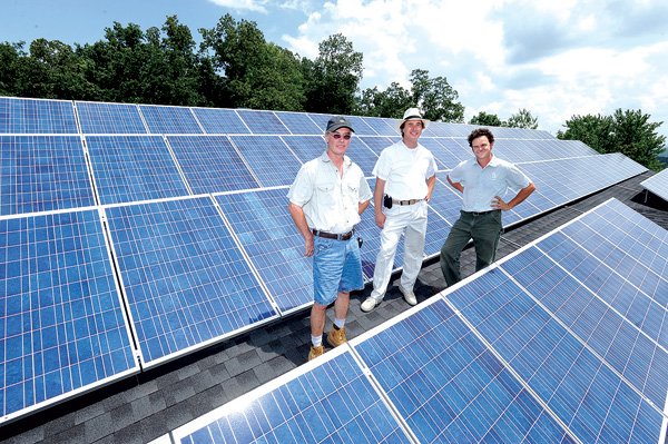 Jack Besser, from left, owner of Besser Electric; Stephan Pollard, chief executive officer of Trem|Wel Energy; and Flint Richter, lead installer of photovoltaic panels for Rocky Grove Sun Company in Kingston stand on the roof of a house at 680 Cliffside Drive in Fayetteville on Wednesday as the trio continues installing an array of solar panels and connect it to the house’s electric service. The installation is the largest residential solar panel array in the state.