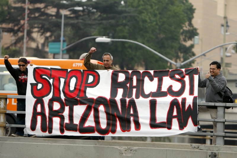 From left, Franchezska Zamora, Hamid Khan, and Ken Montengearo, pro-immigration activists hang a banner from a freeway overpass protesting Arizona's anti-illegal immigration law during the rush hour commute in downtown Los Angeles,  Monday.