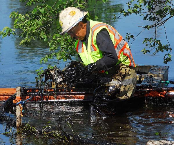 A worker lifts oily debris from the Kalamazoo River on Tuesday in Battle Creek, Mich.