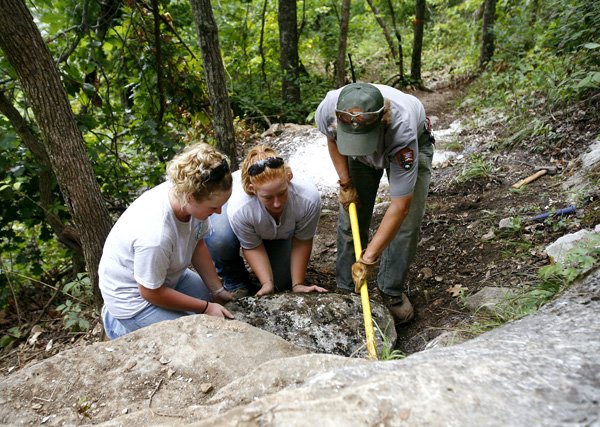 Youth Conservation Corps participants (from left) Andrea Edgmon, 17, of Deer and Kimberly Mathis, 18, of Harrison work with trail leader Marilyn Yoniles on Tuesday to position a rock along the Hemmed-In Hollow trail at the Buffalo National River. About 40 students worked with the youth corp for eight weeks this summer on projects at the national river.