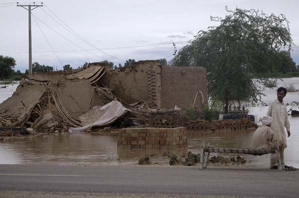 Pakistani villagers gather beside their collapsed house Thursday after flooding on the outskirts of Dera Ismail Khan, Pakistan.