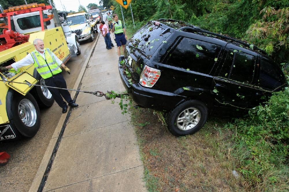Arkansas Democrat-Gazette STATON BREIDENTHAL --9210-- Jimmy Phillips (left) of Phillips Brothers Towing Service pulls a vehicle out of a wooded area at the intersection of JFK Blvd. and Interstate 40 Thursday after the driver lost control of the vehicle and slid off the road. No one was injured in the one vehicle accident.