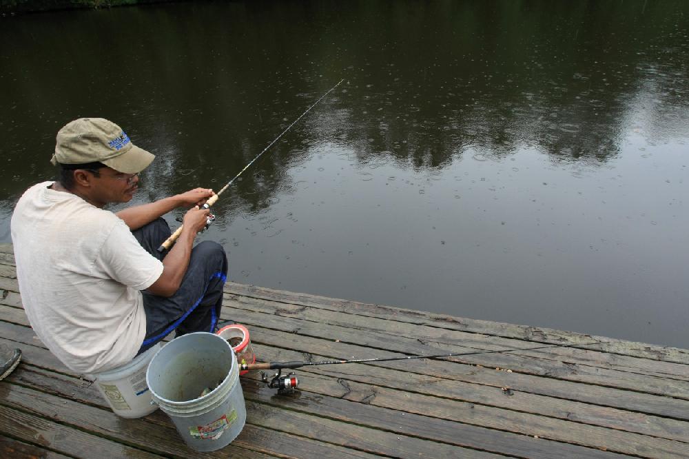 Arkansas Democrat-Gazette STATON BREIDENTHAL --9210-- Kevin Burrell uses a bucket for a seat Thursday afternoon while fishing in the rain in the Lakewood area of North Little Rock.