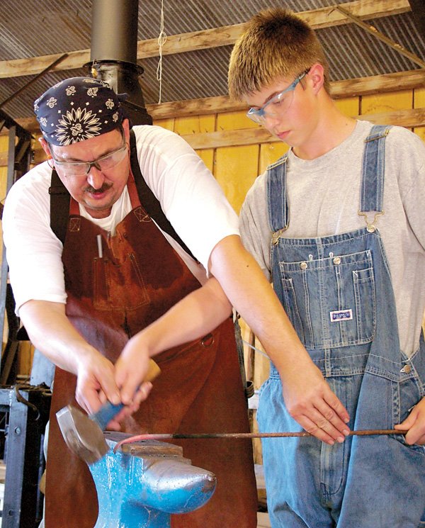 R.J. Barnica, 12, takes a lesson from master blacksmith Dale Custer in the blacksmith shop at the Tired Iron of the Ozarks show grounds on Saturday.
