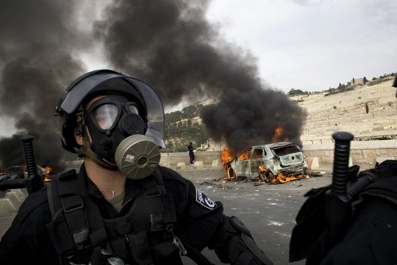 An Israeli police officer wearing a gas mask walks past a car set on fire by Palestinian rioters during clashes outside Jerusalem's Old City, Wednesday.