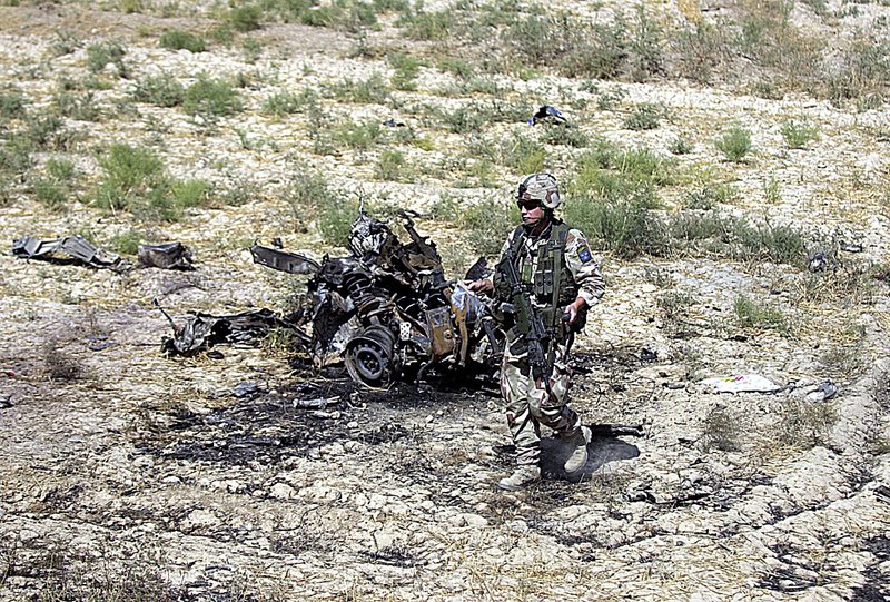 A NATO soldier stands Friday near the remains of a suicide bomber’s vehicle outside Mazar-i-Sharif, Afghanistan. The convoy targeted in the attack was only slightly damaged, but the blast killed a child and injured at least 28 people in a bus that was passing by. 