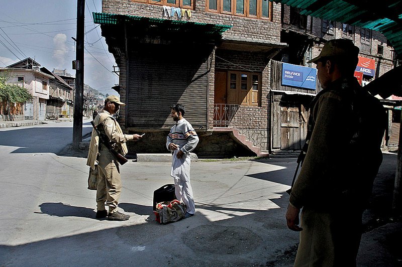 An Indian paramilitary soldier checks the identity card of a civilian during curfew Saturday in Srinagar, India.