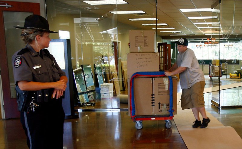 Benton County Cpl. Kristina Bertschy (left) watches as workers move furniture out of the Pinnacle Investments office building on Wednesday in Rogers.