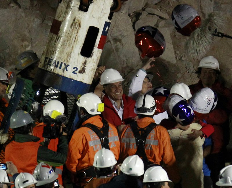 Chile's  President Sebastian Pinera, center, smiles as miner Pedro Cortez, bottom right, is greeted by his family after being rescued from the collapsed San Jose gold and copper mine where he had been trapped with 32 other miners for over two months near Copiapo, Chile, Wednesday Oct. 13, 2010.