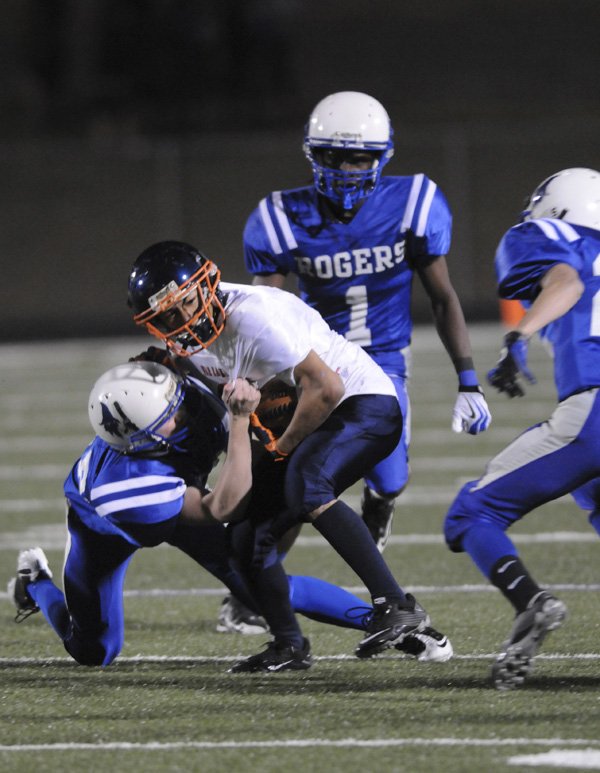 Rogers Heritage’s Carlos Hernandez is pulled down by Rogers High’s defense during the freshman game Thursday in Mounties Stadium.
