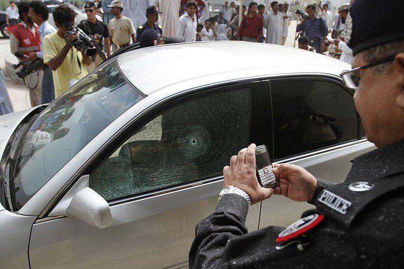 A Pakistani police officer takes pictures of a consulate’s car targeted Thursday by unidentified gunmen in Karachi. 