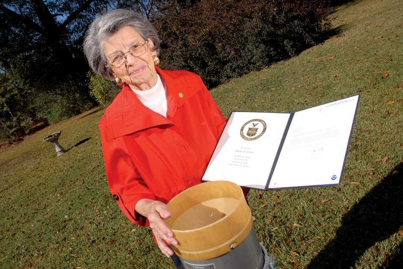 Louise Yates received an award from the National Weather Service for 45 years of weather observations at her home in Bismarck. She stands by the rain gauge she uses for measurements.