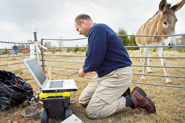 Scott Ausbrooks, a geologist for the Arkansas Geological Survey, downloads monthly data from a seismic station to his laptop on a Faulkner County farm. Ausbrooks monitors many such stations in the region.