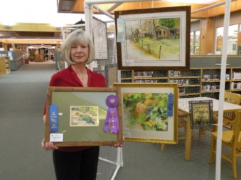 Sandra Ake of Conway shows the awards she won in the Conway League of Artists’ Tri-County Art Show. She received first place in the Water-Based Paint category and Best in Show for the watercolor painting she is holding, titled Collared Lizard. She received the Jackie Guerin Beauty in Nature Memorial Award for her watercolor Pumpkin Patch, shown at right. A third watercolor by Ake, Rush Ghost Town, shown above, won an Honorable Mention in the Water-Based Paint category.