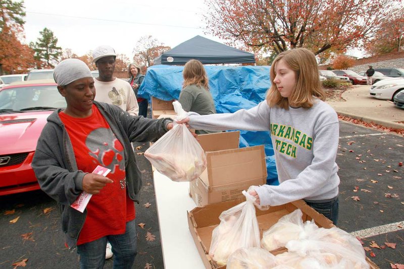 Volunteer Julia Bush, 14, hands a frozen hen Tuesday to Sherese Young and a box of food for a Thanksgiving meal at the Agape Church in Little Rock, at 701 Napa Valley Drive. 