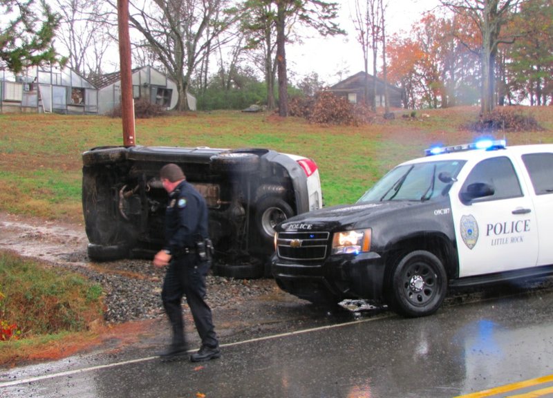 A Little Rock Police Department officer walks by an overturned SUV on Bowman Road Thursday.