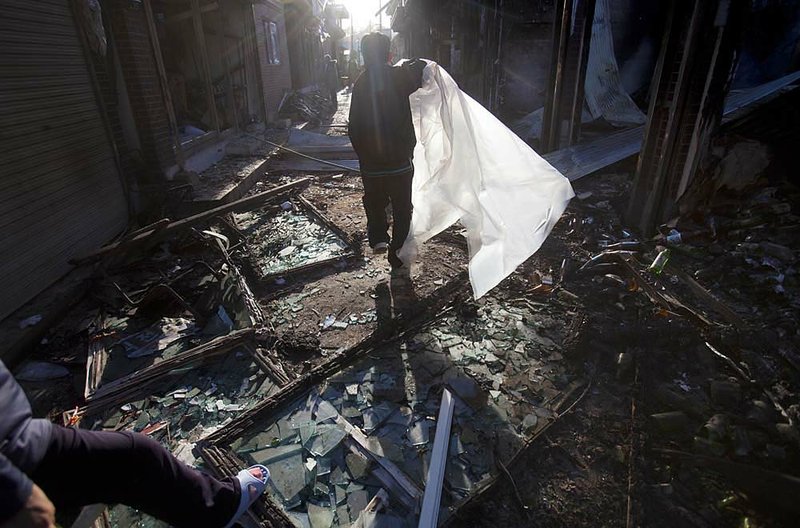 A resident of South Korea’s Yeonpyeong Island walks through ruins Thursday with a plastic sheet to cover windows shattered in North Korea’s attack on Tuesday. 