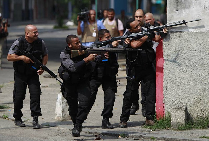 Policemen aim their weapons as they take cover from gunfire Thursday during an operation against drug traffickers at the Vila Cruzeiro slum in Rio de Janeiro, Brazil. 