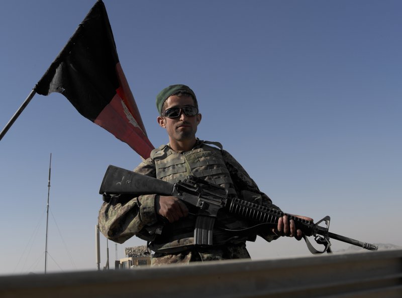 An Afghan national Army soldier attached to First Battalion, 502nd Infantry Regiment, 101st Airborne Division stands atop of military track before patrolling in Panjwai district, Afghanistan's Kandahar province, Saturday, Nov. 27, 2010, with an Afghan national flag at the background. (AP Photo/Alexander Zemlianichenko)