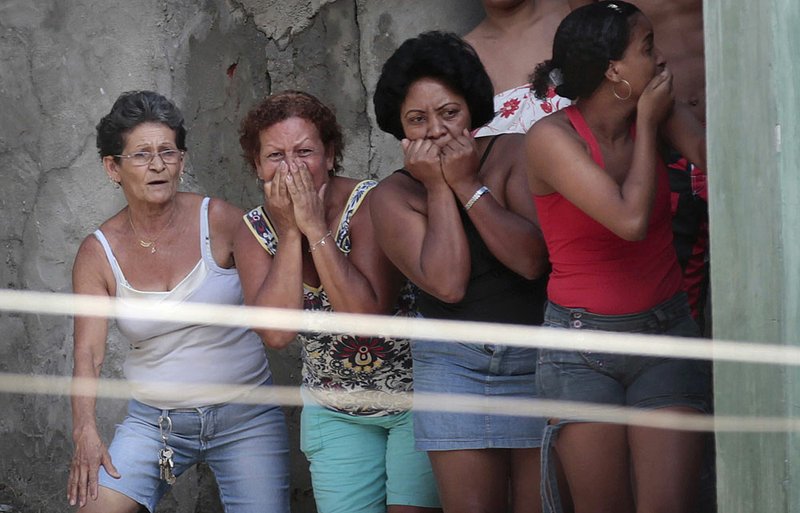 Women watch after a shooting set a house on fire in the Alemao slum complex in Rio de Janeiro where soldiers and police have drug-gang members cornered in advance of an expected assault to drive the criminals out. 