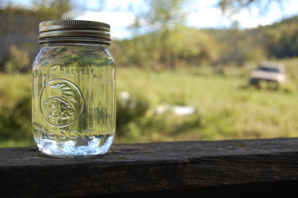 At the end of a long gravel road where a still is hidden in a barn, a lone Mason jar of fresh moonshine sits atop a fence rail.