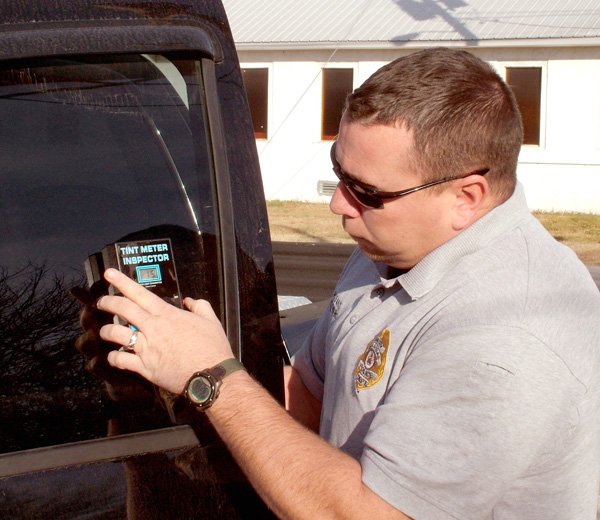 Sgt. Clay Stewart of the Gentry Police Department demonstrates the use of a tint meter on side window glass last week. State law requires front seat side windows to allow a minimum of 25 percent of the light to pass through. Rear side windows must allow 10 percent of light to pass through. Many windows are tinted too dark and restrict vision to the point of causing a driver not to be able to see other traffic or pedestrians.
