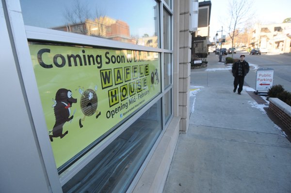 Stephen Rego walks toward a banner Thursday announcing the coming of a Waffle House to Dickson Street in Fayetteville. Rego works on Dickson Street and thinks Waffle House coming to Dickson Street is a good idea.