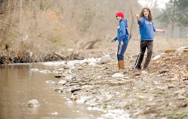 Miah Schultz, 11, and friend Sophie Harris, 11, skip rocks Saturday at Niokaska Creek in Sweetbriar Park in Fayetteville. The city accepted bids last month to reconstruct the eroded stream bank along the waterway in the Illinois River watershed.
