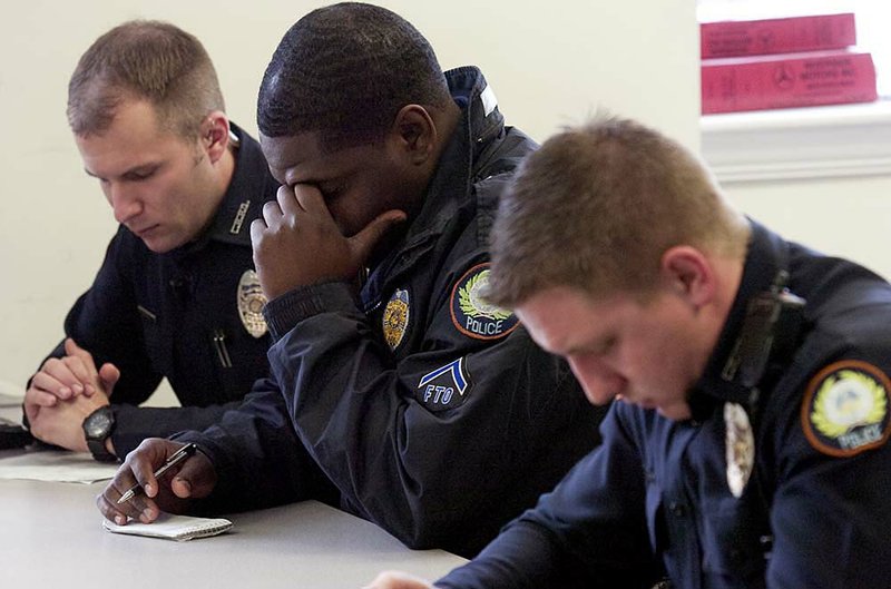 Little Rock police officers Aaron McDurmont (from left), Byron Harper and Renar Benson bow their heads as the Rev. Ken Martin leads them in prayer before the starts of their shifts.

