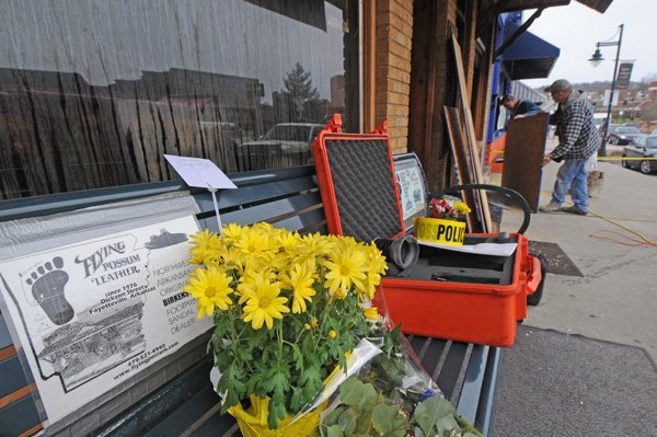 Joe Baird of Fayetteville and T.R. Sutton of Elkins board up the windows of Flying Possum Leather on Dickson Street on Monday. An early morning fire claimed the life of the owner Bruce Walker. Memorial flowers share a bench outside the business with a fire marshal’s investigative gear case.