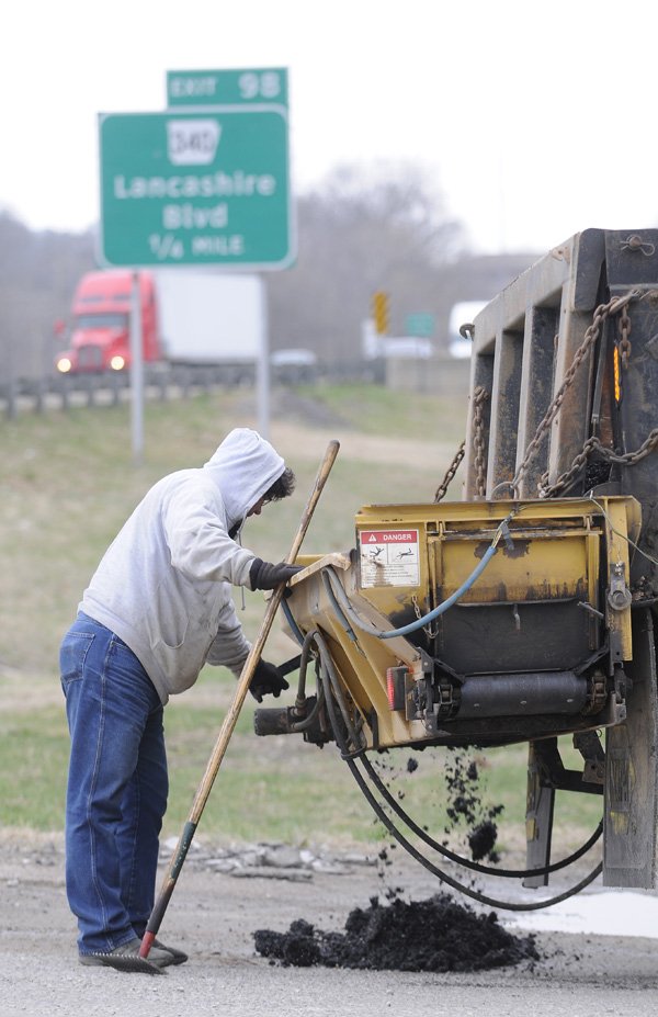 Tim Fosdick, with the Bella Vista Property Owners Association’s Street Department, drops asphalt into a pothole Wednesday in Bella Vista. The association could be fined by the Arkansas Contractors Licensing Board for performing contract work without a license.