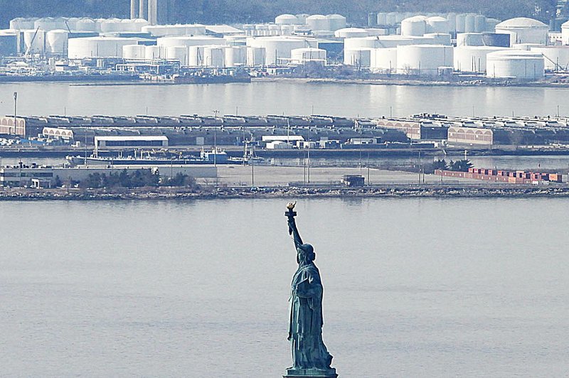 The Statue of Liberty stands in New York Harbor on Tuesday with an oil-storage facility in the background. Oil prices fell sharply Tuesday on fears about Japan’s economy. 