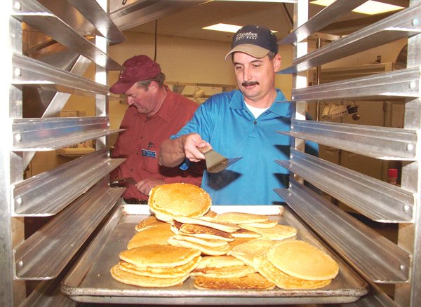 Lions Club member Mark Burden tosses pancakes from the griddle onto the serving pan during the annual pancake supper on Thursday in Gentry. Terrell Shields is frying pancakes in the background. Proceeds raised by the club are used to pay for eye glasses and eye procedures for those who cannot afford them.