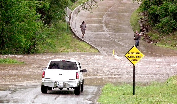 A woman standing on the opposite bank motions and shouts for the driver of the pickup truck to “go around” rather than drive through the storm waters. Flood waters covered Grant Street in Decatur, blocking the entrance to the apartments at the end of the street. Many other roads and highways were closed for a time on Tuesday as record rainfall amounts created raging rivers which overflowed roadways.