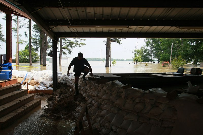   Flood waters from the White River and surrounding oxbow lakes flood homes near Holly Grove Monday. Danny Singleton climbs from his boat and over a sandbag levee around the home of John Devine on East Lake. Singleton and Neal Skipper were bringing him a sump pump.