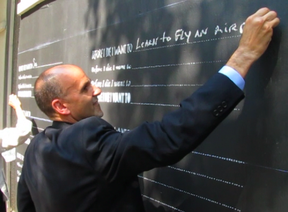 Chuck Spohn, president of the board of directors for the Downtown Little Rock Partnership, adds his entry to a new public art project on a Main Street wall asking passersby to write in chalk in what they want to do before they die.