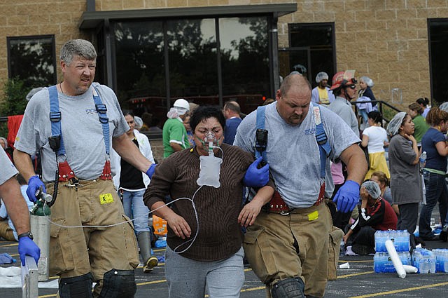 Springdale firefighters help a woman to an ambulance outside the Tyson Foods plant on Berry Street in Springdale on Monday morning. A chlorine leak evacuated the plant and sent more than 20 employees to area hospitals at about 9:15 am Monday.