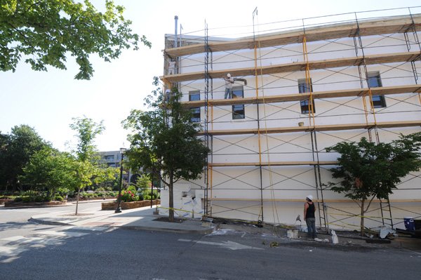 Workers prepare the west wall of the building on the south side of the Fayetteville square for stucco Tuesday. The native limestone along with an old Coca-Cola advertisement are in the process of being covered at the behest of the building’s owner.