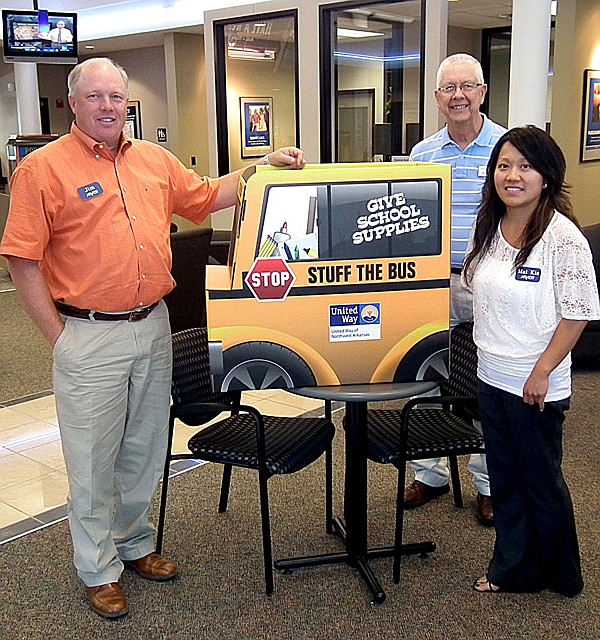 Jerry Cavness, area United Way coordinator, placed a stuff the bus collection box in the lobby of the Arvest Bank in Gravette. Pictured on the left is bank president Jim Singleton and on the right is financial services representative Mai Kia Vang-Thao. United Way is collecting school supplies for students in need in Gravette and Decatur. Arvest Bank is one of many collection sites.