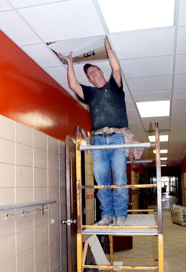 Larry Weihe installs a ceiling tile panel in the hallway at Glenn Duffy Elementary School in Gravette.